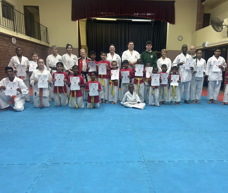 Junior and senior students holding grading certificates in the dojo, June 2025
